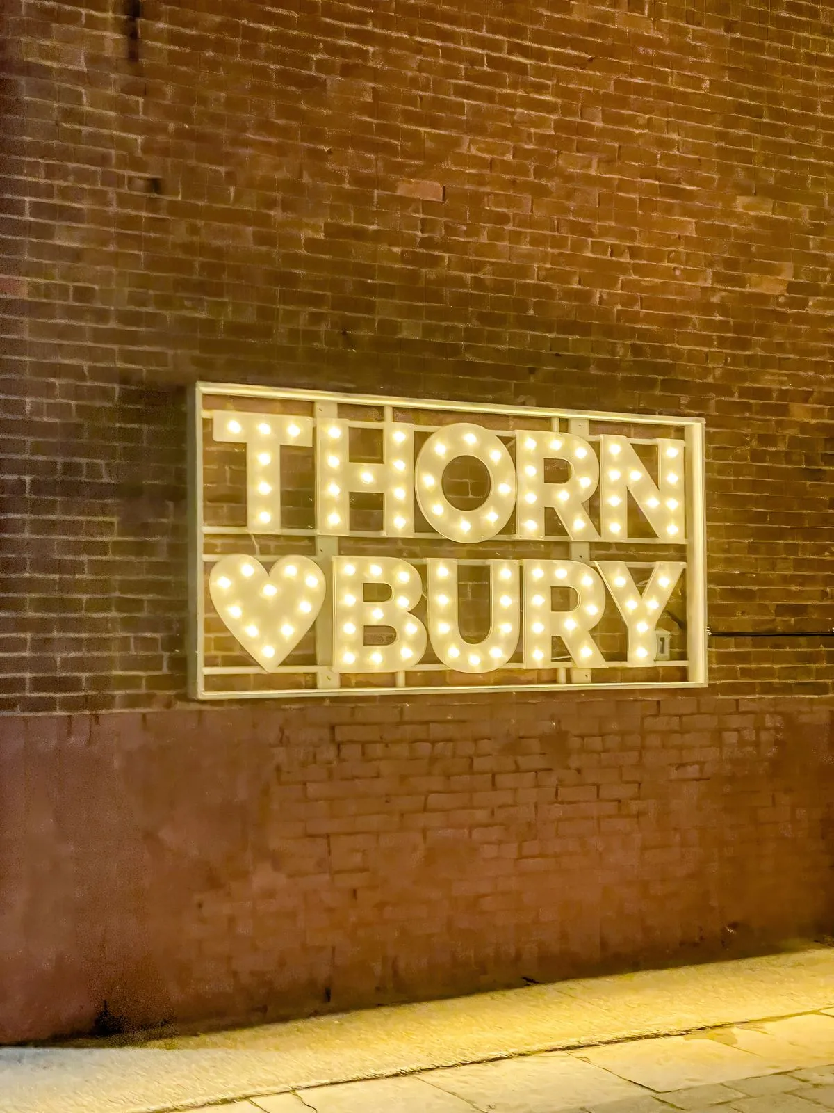 An illuminated marquee sign with bulb letters and a lit heart, mounted on a brick wall at night